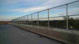 Tall, custom chain link railing atop cement wall. Cedar Rapids fence company commercial fencing contractors Cedar Rapids, Iowa commercial industrial high security correctional recreational sport ballfield tennis court basketball pickleball football stadium track high school college playground manufacturing prison cell tower chain link barbwire gate posts tubing pipe top rail chain link fabric wire mesh galvanized aluminum vinyl coated black brown green 9 gauge fence fencing security perimeter razor concertina wire hinges installation repair costs panels hardware fittings 